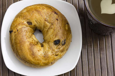 A delicious raisin cinnamon bagel and hot drink with heart shaped milk decorationの写真素材