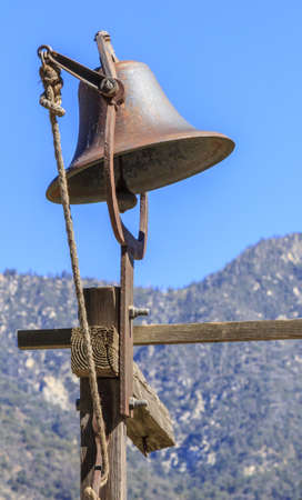 A rusted bell on a wood frame in a farm overlooking the mountainsの写真素材