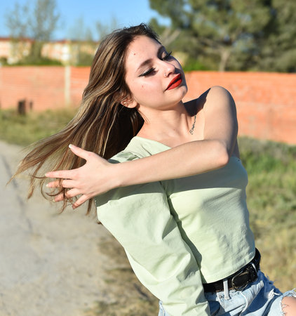 Young woman with long hair and blue jeans posing outdoor in sunny dayの写真素材