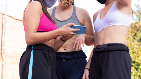 Three unknown girls wearing masks look at a picture of a mobile phone while practicing basketball on...