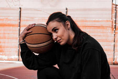 The basketball player wears a black sweatshirt while resting her head on the ball.
