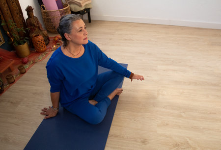 middle-aged yoga teacher sits on her mat while supervising her students in a private class.の写真素材