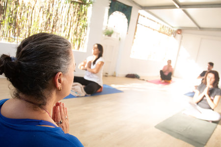 the middle-aged yoga teacher is praying on her mat while supervising her students who are performing the same movements as her.の写真素材