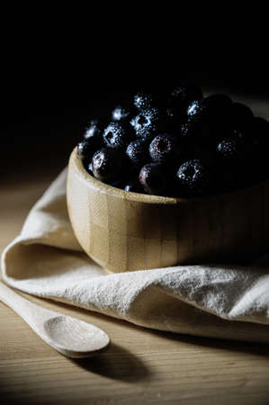 Fresh blueberries with small drops of water on the surface, in a bamboo bowl on a wooden table, with...