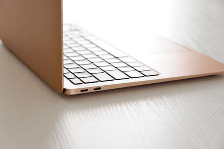 Gold laptop, incredibly thin, light and perfectly portable notebook open on a white wooden table, with light from behind.の写真素材