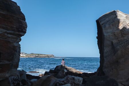 Symetric shape with a solitary man in the middle of two massive rocks by the water