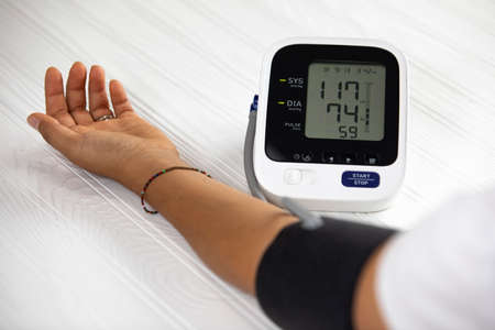 Woman measuring his own blood pressure, white wood