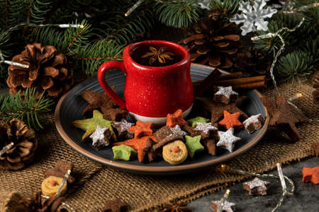 Hot tea on a red cup and Christmas cookies with a star and snowman shape. Decorated with natural pine branchesの写真素材