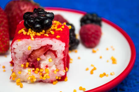 Sweet and delicious red sushi with blackberries, strawberries and sesame seeds on a white plate with red frame on blue background.の写真素材