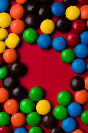 Frame of red, brown, blue, green, yellow and orange candy with a free space for text on a red background.の写真素材