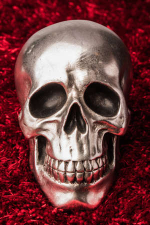 Front view of a silver skull with marks and shadows on red rug background.の写真素材