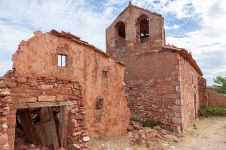 Ruins of a house of red stone, near a church in an abandoned villageの写真素材