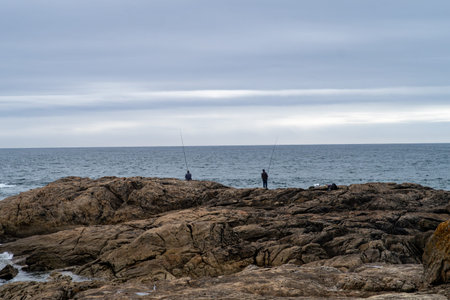 Fishermen fishing on a rock in the sea on a cloudy day