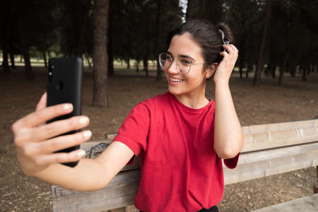 Young attractive woman talking through the phone and smiling in a park, sit down in a benchの写真素材