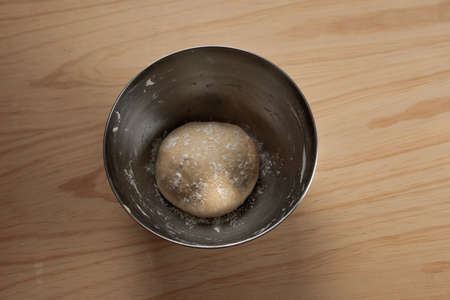 Overhead view of the hands of an adult woman kneading pizza dough in a wooden table in the kitchen
