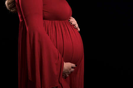 Unrecognizable pregnant woman holding tiny woolen shoes over the belly for an expecting babyの写真素材
