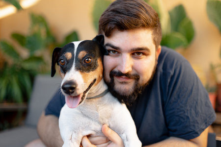Friendly young man hugging his cute grocer dog with both hands while looking at him, the dog has the tongue out while looking at cameraの写真素材