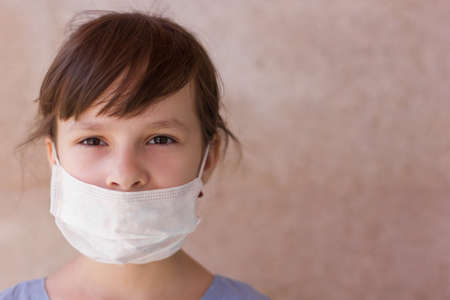 Portrait of a young girl in a medical mask isolated on a wall background. Young woman patient, copy spaceの写真素材