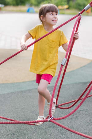 Adorable 6 years old girl in the yellow t-shirt on the playground.の写真素材