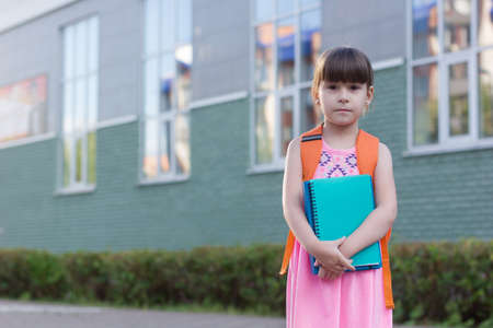 Cute little schoolgirl with backpack holding notebooks on the yardの写真素材