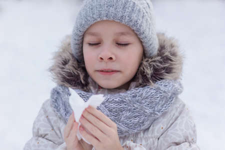 Girl with allergy symptom blowing nose. Teen girl using a tissue in a winter park.