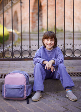 Happy young girl sitting on the ground in the city near her backpackの写真素材