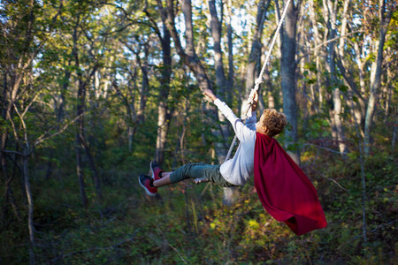 A boy on a rope swing in a red raincoatの写真素材