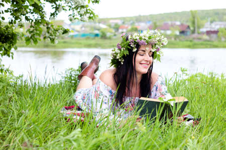 a young woman in a wreath reads a book sitting on the grassの写真素材