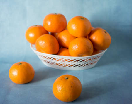 Ripe tangerines in a white bowl on a blue background