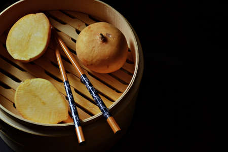 Bamboo steamer, turnips, and chopsticks isolated on black backgroundの写真素材