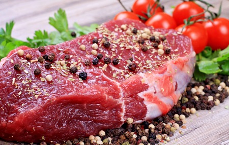 Raw beefsteak with spices and cherry tomatoes on wooden backgroundの写真素材