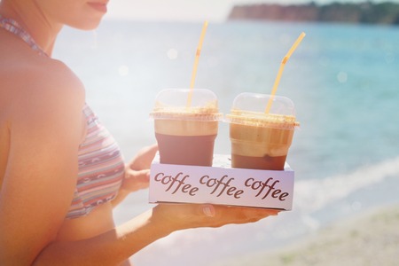 Attractive female waiters holding two ice frappe coffee on the beach near sea. Young woman enjoyng during summer holiday, vacation on tropical resort by ocean.の写真素材