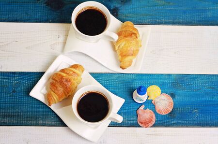 Two cups of coffee , croissants and flowers on white and blue rustic marine background. Vacation breakfast conceptの写真素材