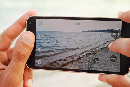 Close up on male hands taking photo of sea coast with mobile cell phone. Summer beach holiday vacation conceptの写真素材