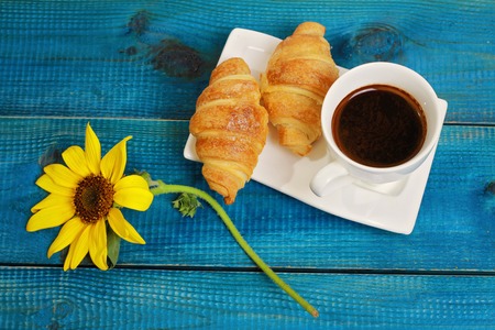 Coffee , croissants and sunflower on blue rustic wooden background. Autumn, vacation breakfast conceptの写真素材