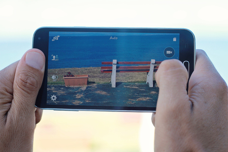 Close up on male hands taking photo of sea coast with mobile cell phone. Summer beach holiday vacation conceptの写真素材