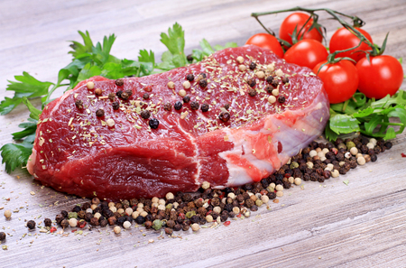 Raw beefsteak with spices and cherry tomatoes on wooden backgroundの写真素材