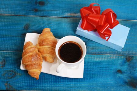 Cup of Coffee , croissants and present, gift on blue rustic wooden background. Romantic vacation breakfast conceptの写真素材
