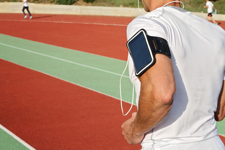 Man running down stadium track. Male runner  listening to music on mp3 player or mobile phoneの写真素材