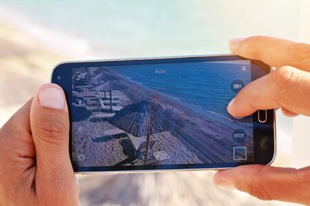 Close up on male hands taking photo of sea coast with mobile cell phone. Summer beach holiday vacation conceptの写真素材