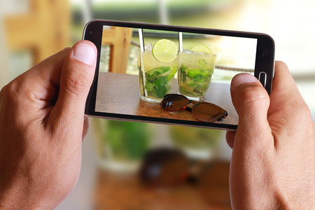 Male hand taking photo of Two fresh mojito cocktails with cell, mobile phone.の写真素材