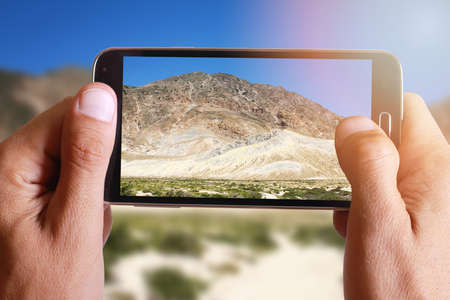 Male hand taking photo of rock mountain landscape with cell, mobile phone.の写真素材