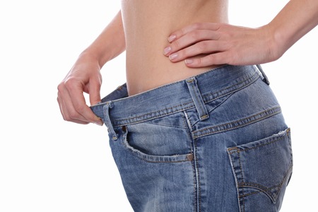 Diet motivation and successful weight loss concept. Close up of slim waist of young woman wearing big jeans on white backgroundの写真素材