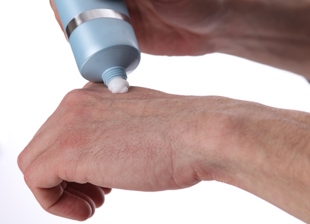 Man applying moisturizer cream on hands, dry skin on white background. Dermatology, cold weather skin care conceptの写真素材