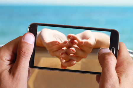 Male hand taking photo on hands of women enjoying summer holiday, vacation with cell, mobile phone.の写真素材