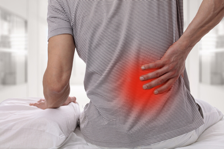Man suffering from back pain at home in the bedroom. Uncomfortable mattress and pillow causes back...