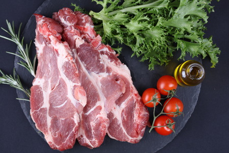 Raw pork neck meat on black background, spices, vegetables, olive oil. Cooking background, healthy...