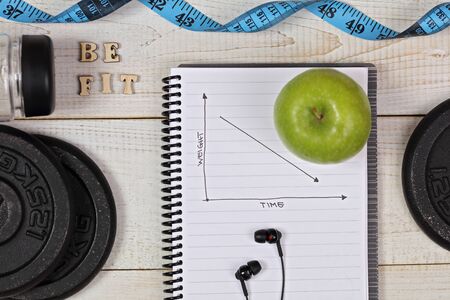 Dieting, Positive weight loss results. Fitness motivation Be Fit. Inspirational quotation. Sport items, dumbbells, apple, bottle of water on white wooden background . Healthy lifestyle concept.の写真素材
