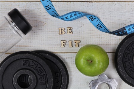 Fitness motivation Be Fit. Inspirational quotation. Sport items, dumbbells, apple, bottle of water on white wooden background . Healthy lifestyle concept.の写真素材