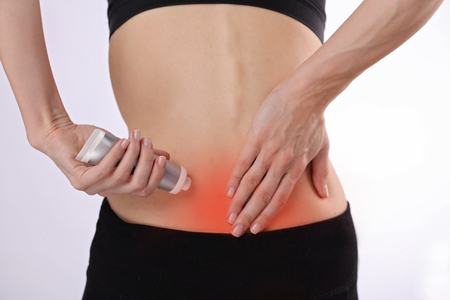 Woman suffering from back pain applying pain relief cream . Sports exercising injury.の写真素材